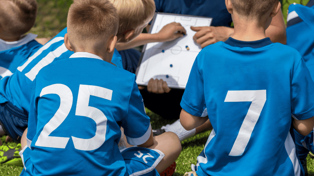 Fußballkinder und Trainer sitzen zusammen und besprechen die Aufstellung mittels Spielfeldplan.